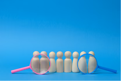 Wooden figurines under pink and blue magnifying glasses on blue surface and background.