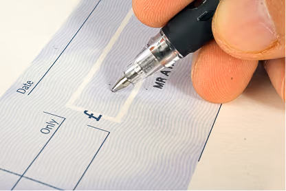 Close-up of a hand holding a pen poised to write on a blank check near the amount box.