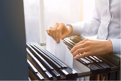 Person filing documents into a black hanging file cabinet with natural light in the background.