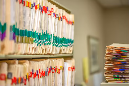 Rows of organized manila folders with colored tabs on shelves and stacked on a table in an office.