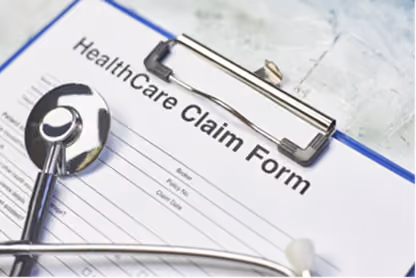 A stethoscope resting on a healthcare claim form on a clipboard over a marble surface.