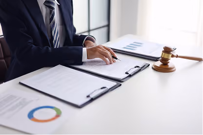 Person in suit reviewing documents at desk with a wooden gavel nearby.