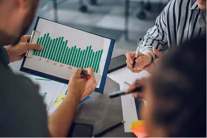Two people examining a clipboard with a green bar graph during a meeting.