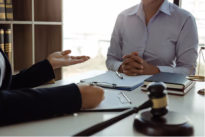 Two professionals in a meeting discussing documents with a gavel on the desk in the foreground.