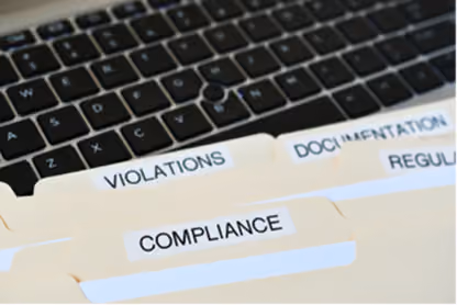 File folders labeled Compliance, Violations, and Documentation on a laptop keyboard.