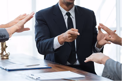 Businessman in suit gesturing with hands during a meeting at a wooden table with documents.