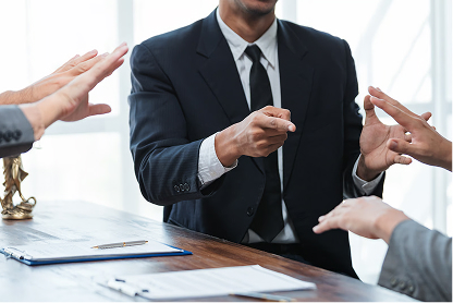 Businessman in suit gesturing with hands during a meeting at a wooden table with documents.