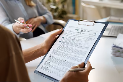Two people reviewing a detailed document on a clipboard in an office setting.