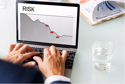 Person typing on laptop showing a risk graph with a descending line on screen.
