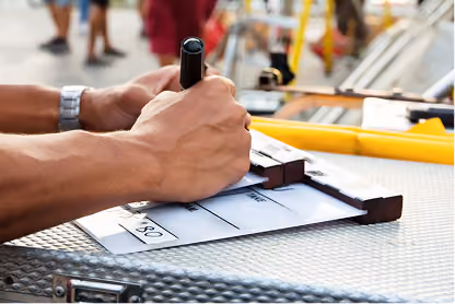 Hands holding a marker writing on a film clapperboard on a textured metallic surface.