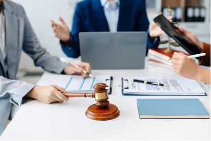 People in a meeting with a gavel on the table, a clipboard, and a laptop in the background.