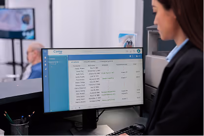 Woman working at desk with computer screen displaying employee attendance and payroll data.