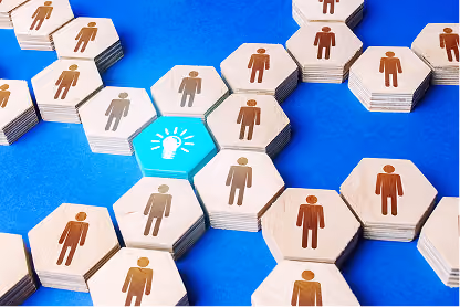 Hexagonal wooden tokens with person icons connected, one bright blue with a light bulb icon.