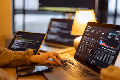 Person working on laptop showing data charts and graphs with a phone and another laptop in background.