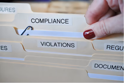 Hand with red nail polish pulling out a file labeled Compliance from a folder with labels Violations and Documents.