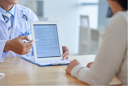 Doctor showing patient a medical form on a tablet during consultation at a desk.