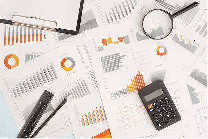 Calculator, magnifying glass, ruler, pencil, and charts with graphs spread on a desk.