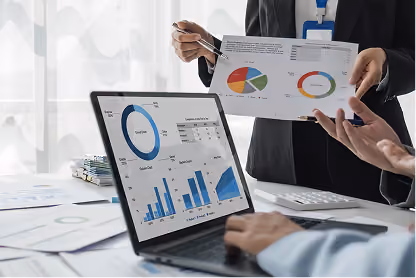Two people reviewing charts and graphs displayed on a laptop and on paper in a business meeting.