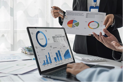 Two people reviewing charts and graphs displayed on a laptop and on paper in a business meeting.