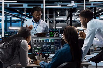 Four engineers collaborating around a computer with a flowchart technical diagram on screen in a lab.