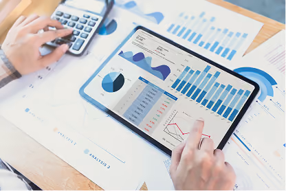 Person using tablet displaying charts and graphs with another hand on a calculator over printed charts.