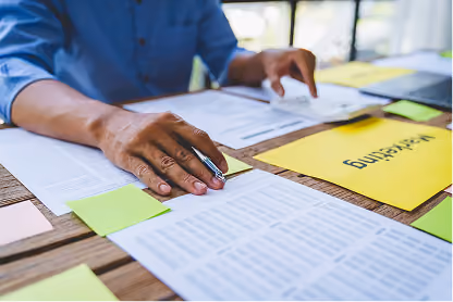 Person organizing documents and colorful sticky notes on a wooden desk for marketing planning.