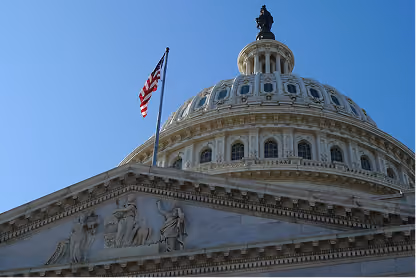 Close-up of the U.S. Capitol dome with American flag and clear blue sky.