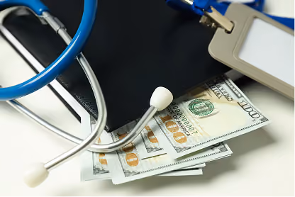 Stethoscope and ID badge resting on a black wallet with several hundred-dollar bills inside.