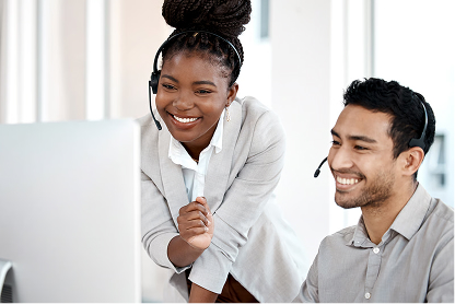 Two smiling customer service representatives wearing headsets looking at a computer screen together.