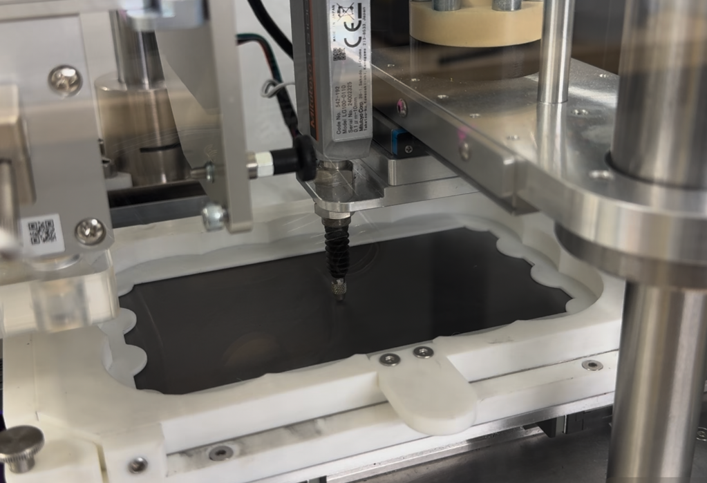 Close-up of a electrode preparation machine measuring the thickness of a black sheet which is electrodes