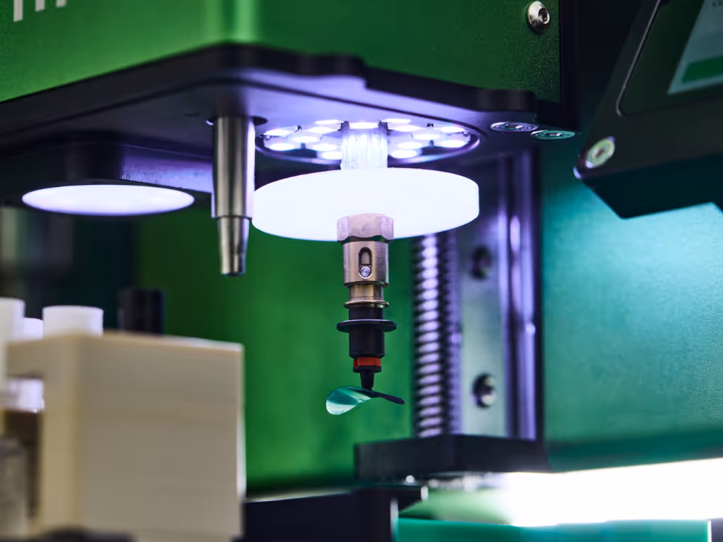 Close-up of a green industrial assembly machine component with a metal nozzle and illuminated circular part.