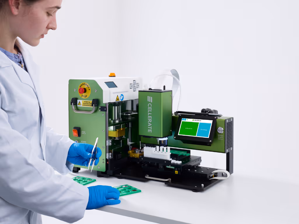 Technician in white coat and blue gloves placing green circuit boards into a green CELLERATE machine with a touchscreen interface on a white table.