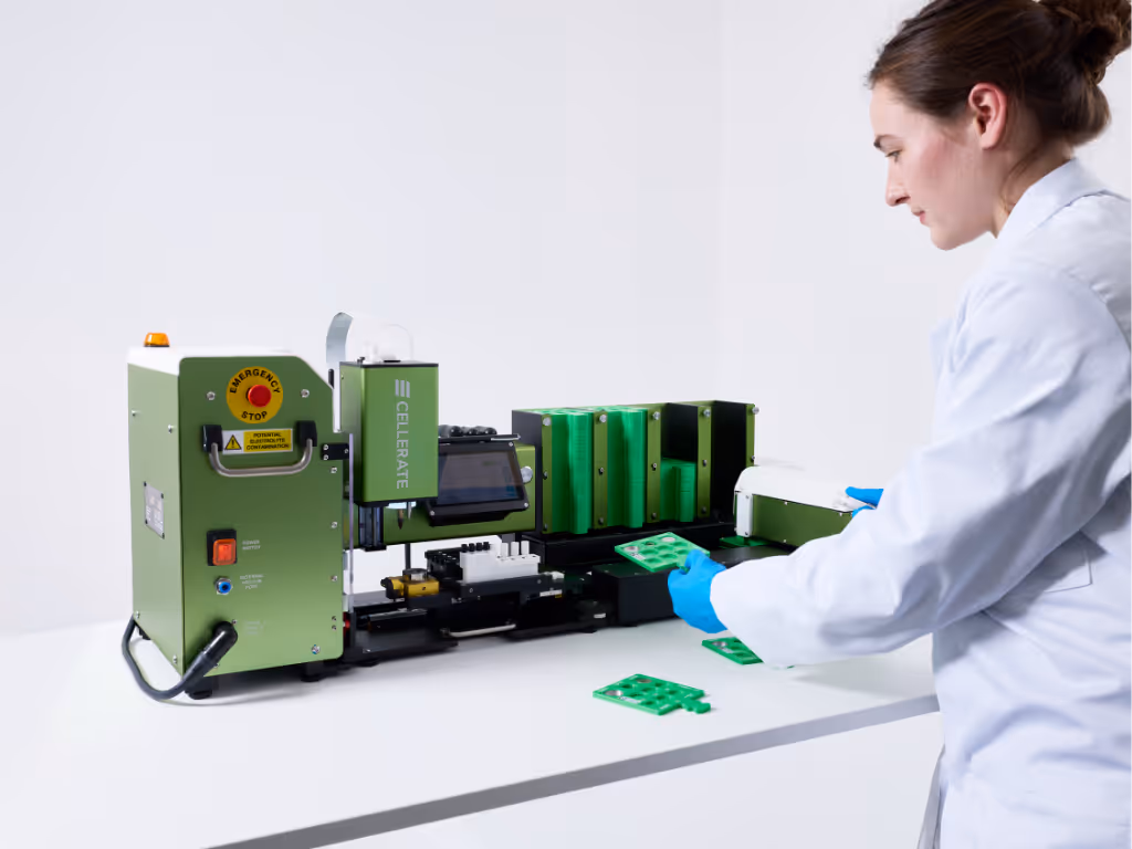 Technician in lab coat and blue gloves loading green cassette trays into CELLERATE machine on white table.