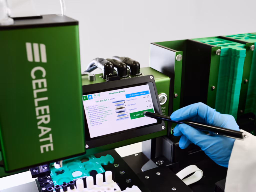 Close-up of a green and black laboratory instrument with a robotic arm and labelled sample tray.