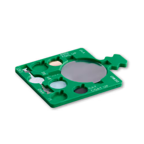 Green plastic protocell tray with multiple circular wells and a central grey reflective disc.