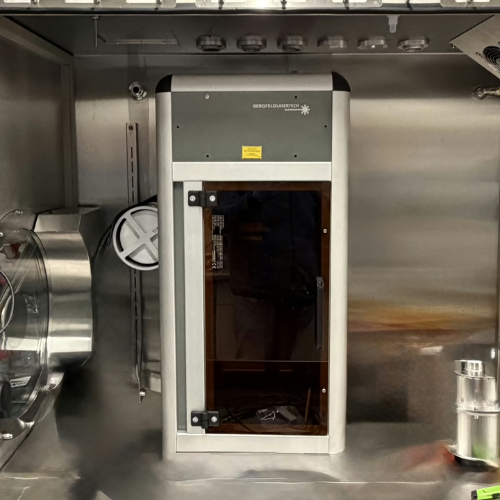 Technician in lab coat and blue gloves loading green cassette trays into CELLERATE machine on white table.