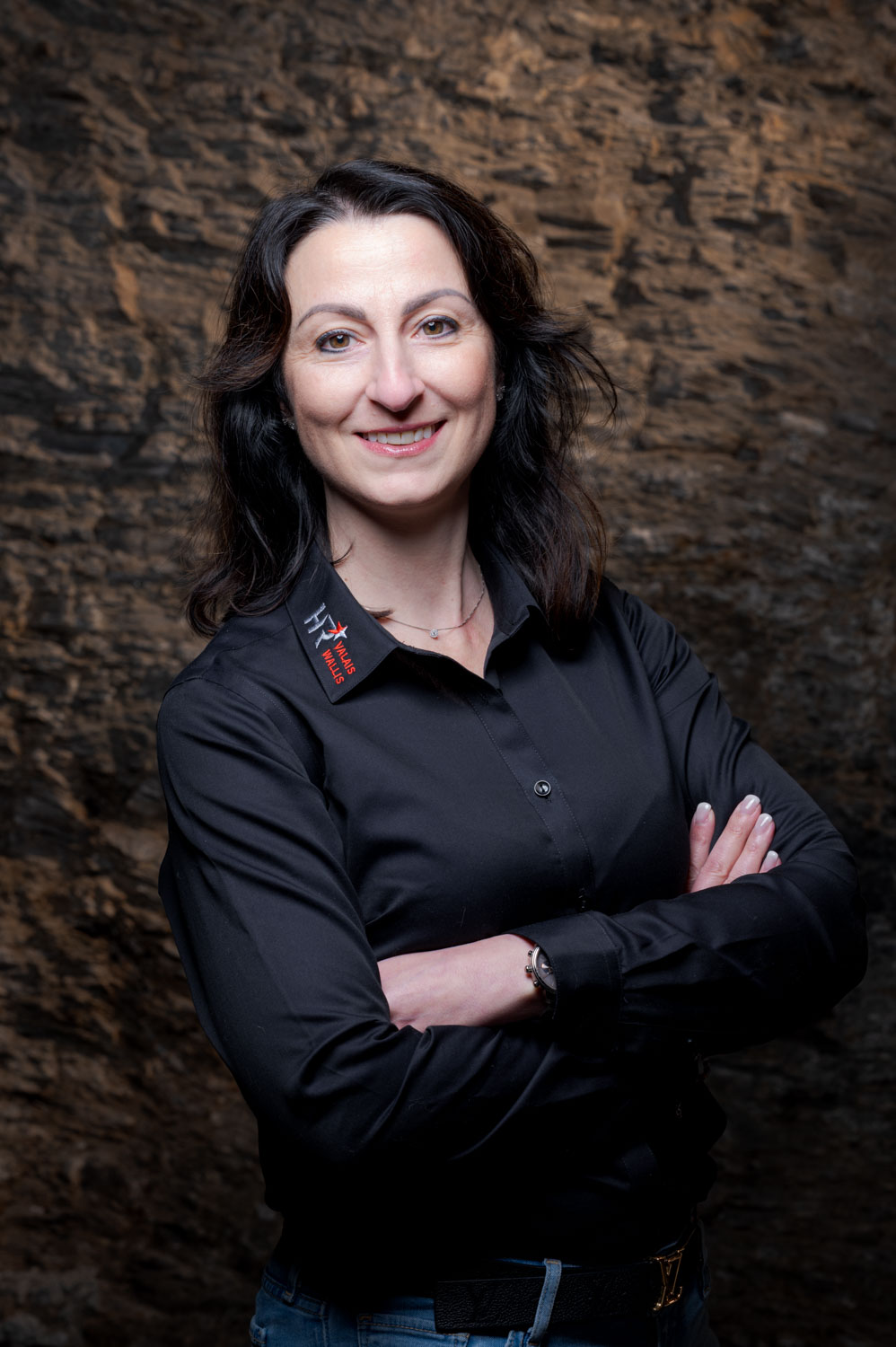 Portrait avec une femme qui croise les bras en abordant un large sourire dans une cave avec un fond de pierre 