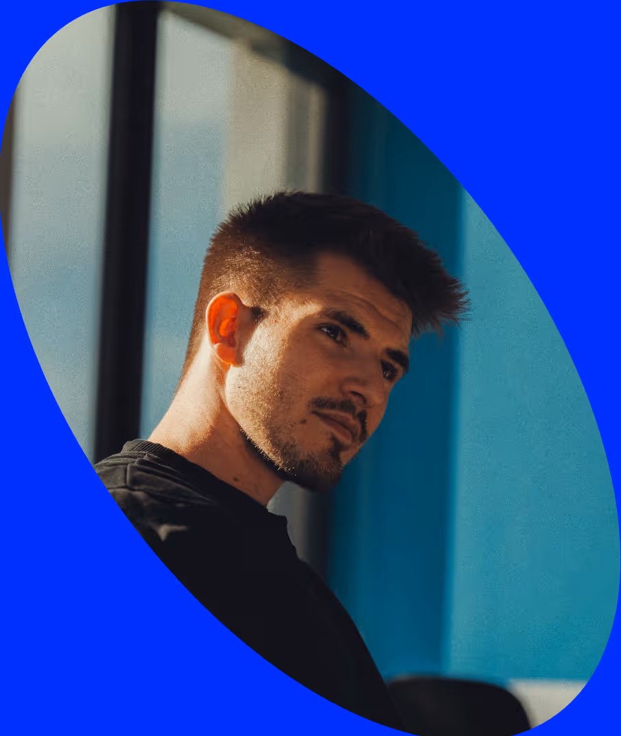 Pensive young man with short hair and beard looking out window in a room with blue walls.