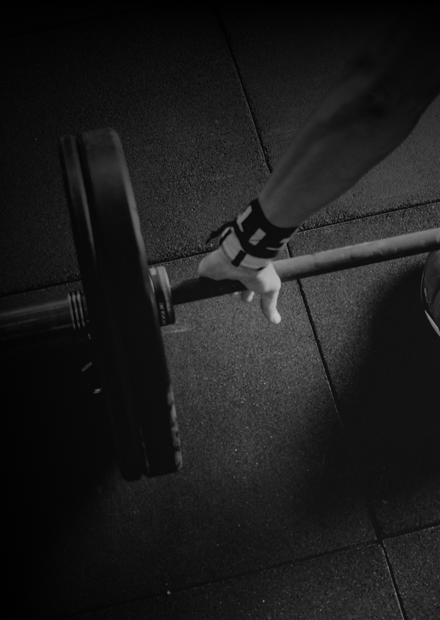 Personal trainer with tattoos wearing a 'STERKERE Personlig trener' shirt coaching a woman exercising on a machine.