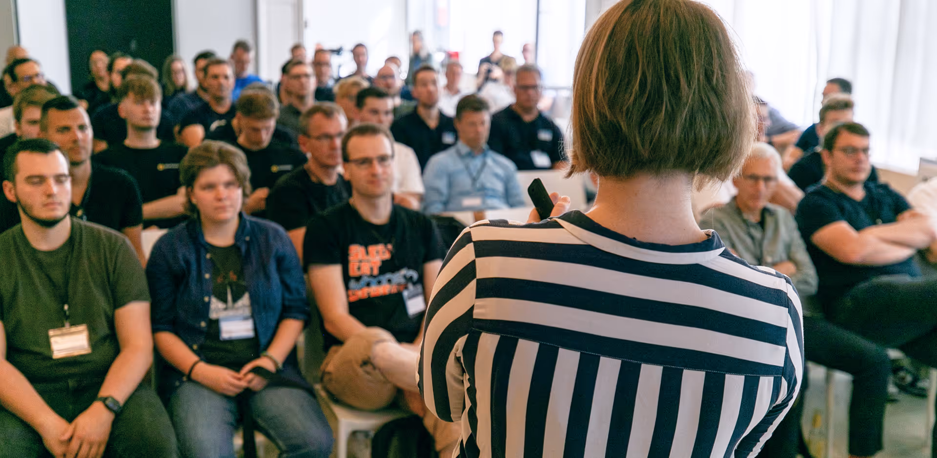 Image of a woman giving a lecture to potential Ninox partners. She is wearing a black and white stripped shirt and she has a short haircut
