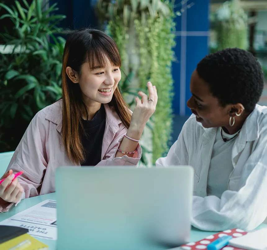 Two women collaborating at a table with a laptop and documents