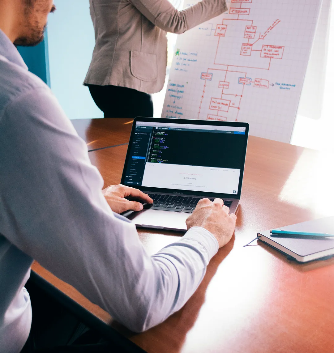 Developer working on a laptop with a process diagram on a board