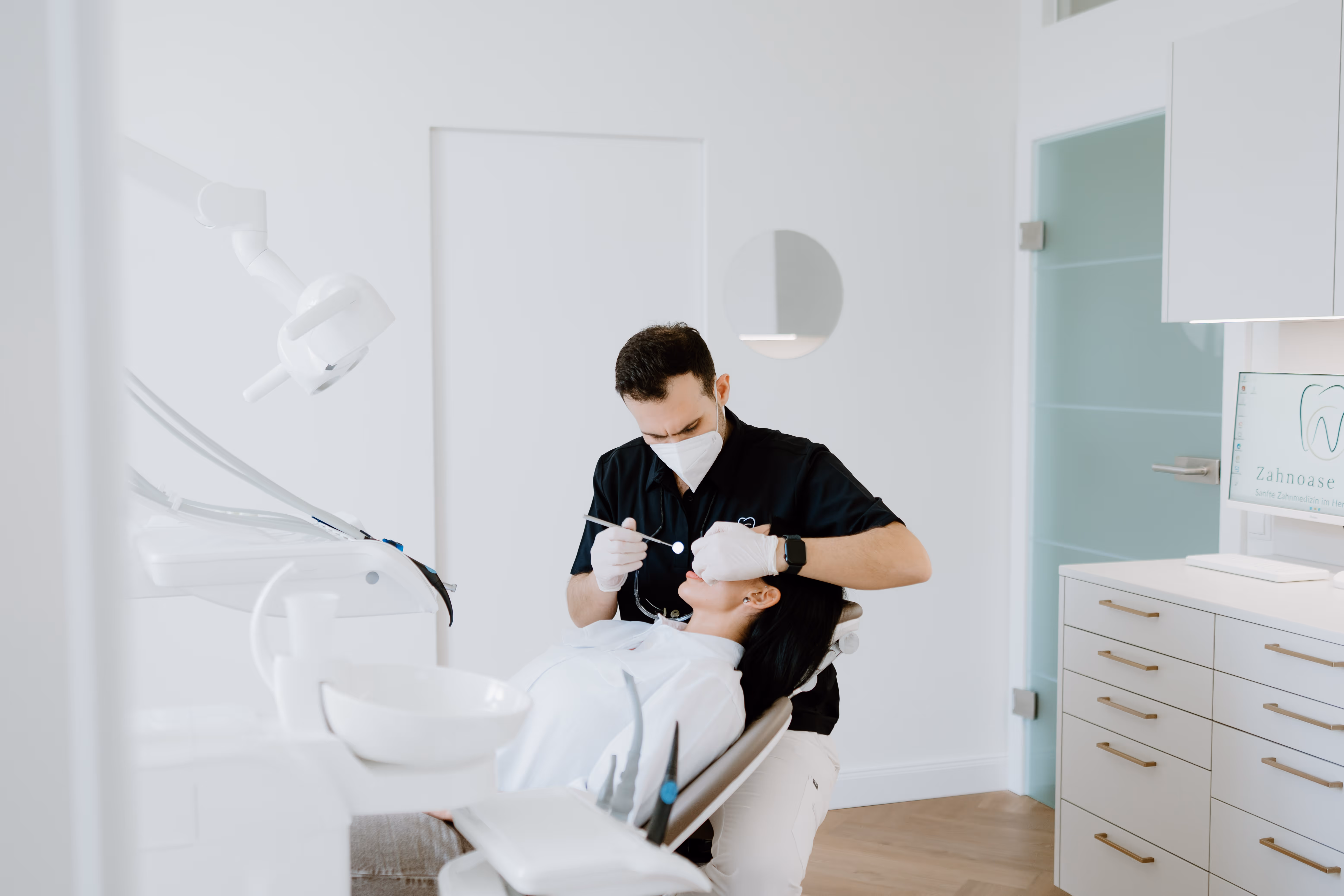Zahnarzt behandelt Patientin in moderner Praxis mit weißer Ausstattung und Holzfußboden.