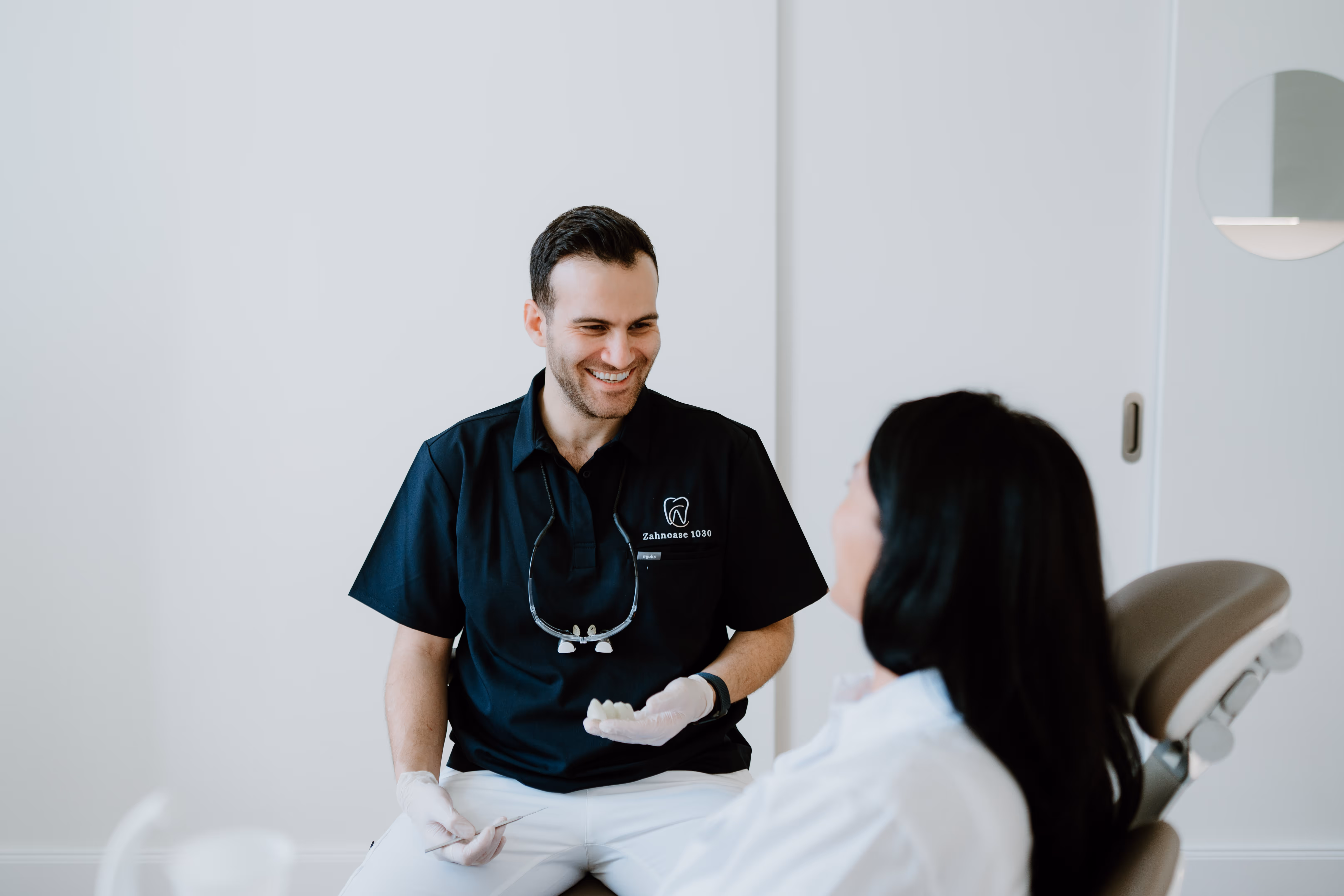 Zahnarzt spricht mit einer Patientin und hält ein Zahnmodell in der Hand.