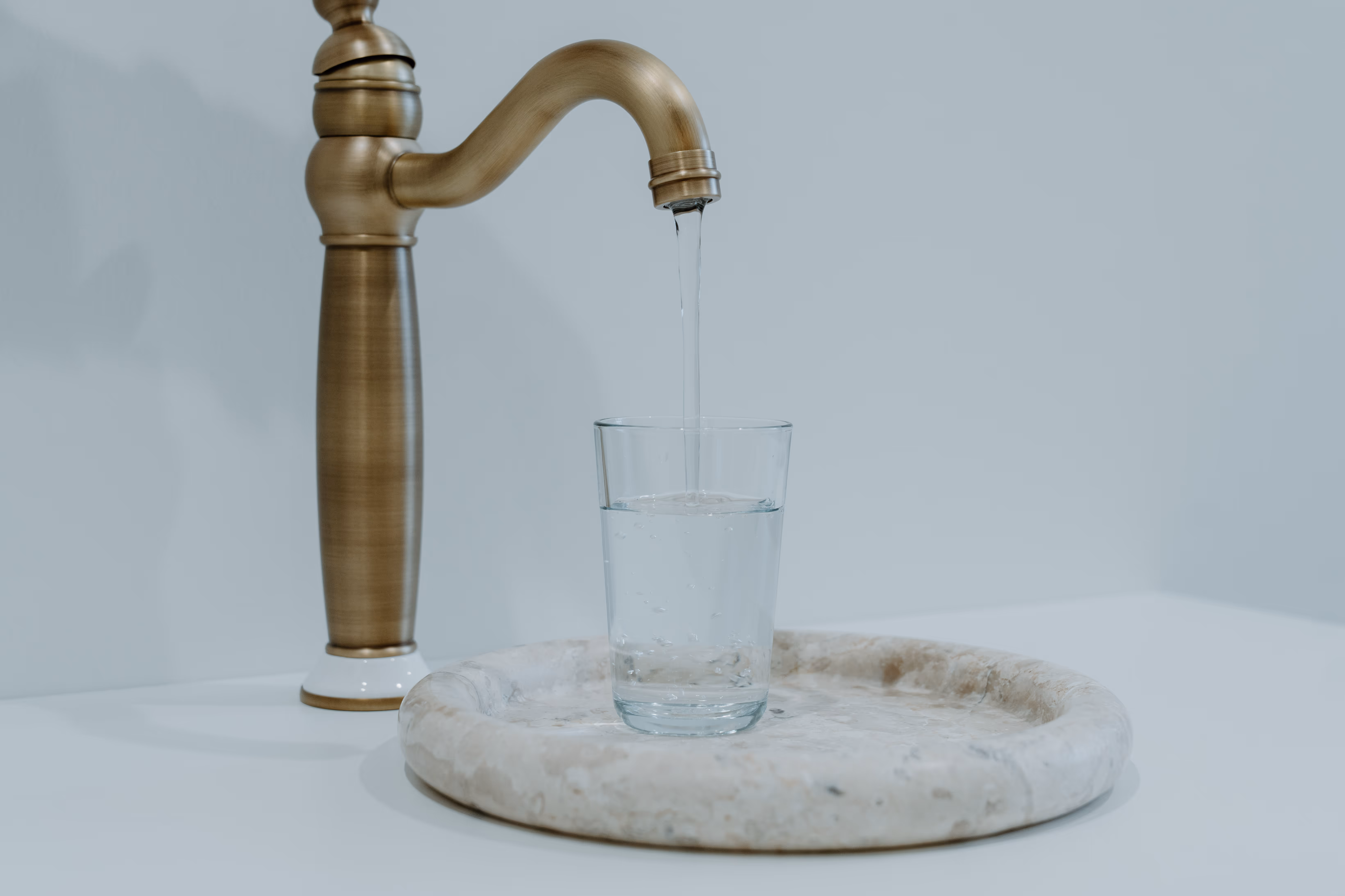 Vintage Wasserhahn, aus dem Wasser in ein Glas auf einem marmornen Tablett fließt.