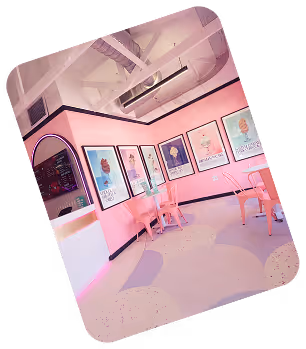 Cozy pink cafe corner with framed colorful posters on the walls and matching pink chairs and white tables.