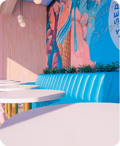 Bright café interior with blue booth seating, white round tables, pink tiled wall, and colorful ice cream mural.
