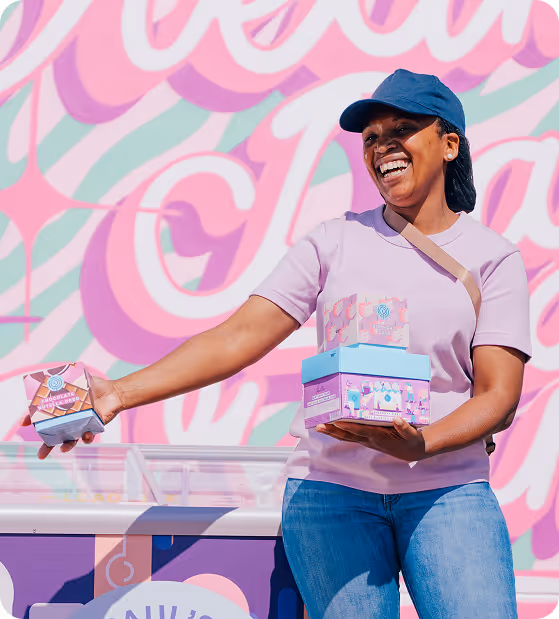 Man in a white t-shirt and jeans holding an ice cream cone up while standing next to a colorful ice cream cart.