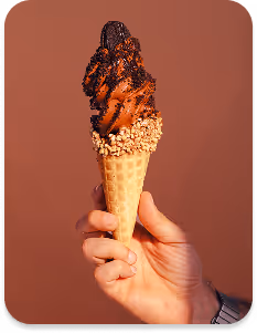 Person wearing gloves dispensing soft serve ice cream into a waffle cone from a machine.