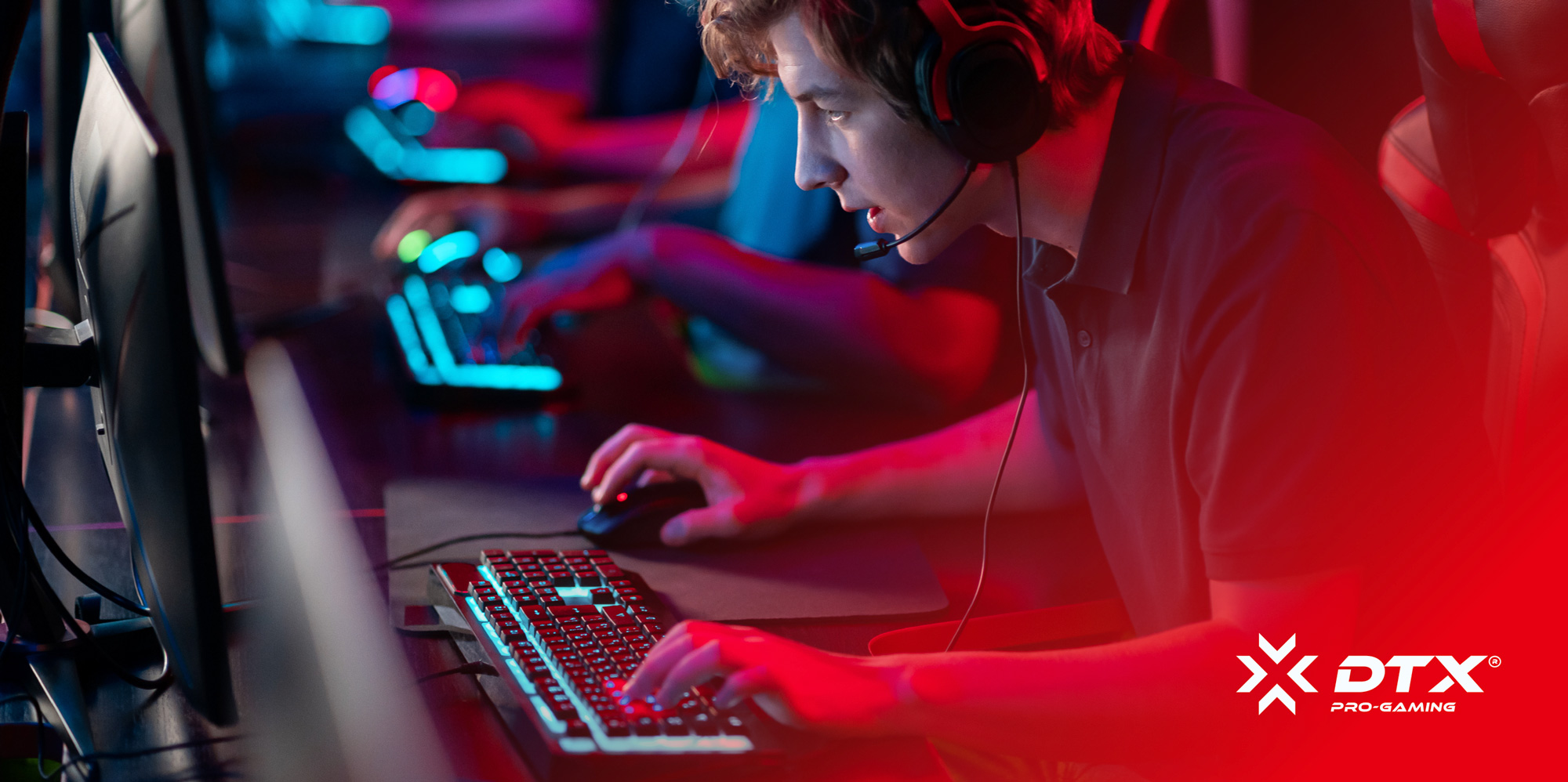 Focused young male gamer wearing headset using keyboard and mouse in a dimly lit gaming setup.